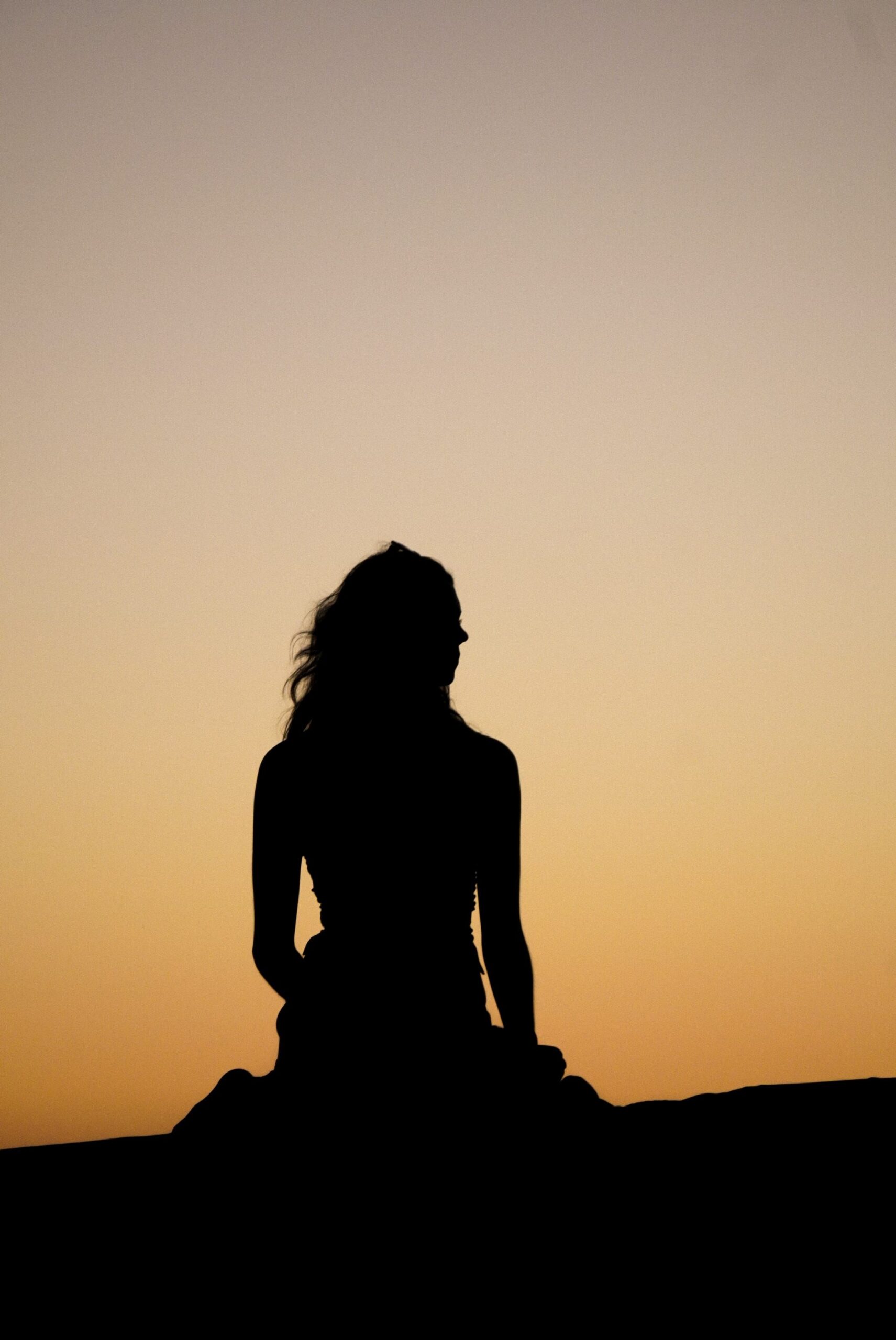 A serene silhouette of a woman sitting against a tranquil sunset sky.
